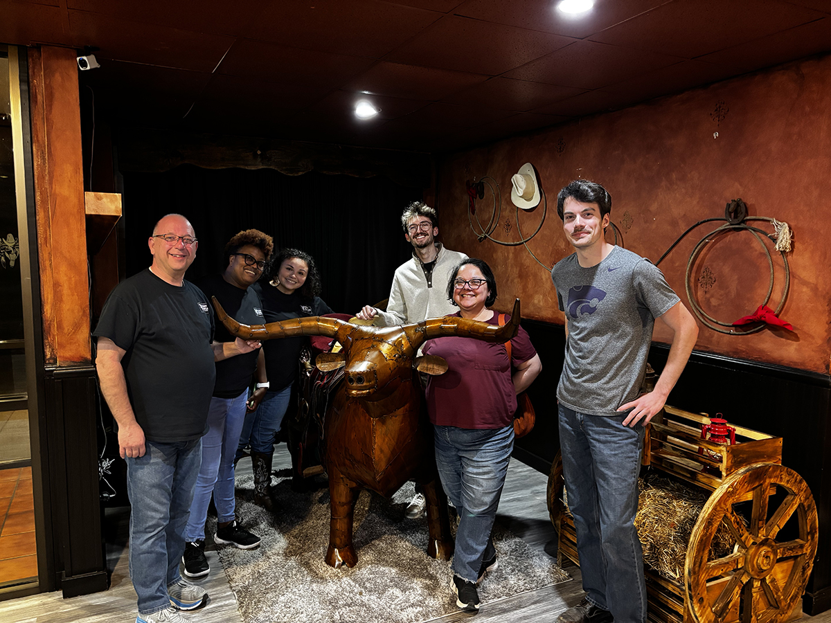 A group of people stand in a room with lassos on the walls with a long-horned bull statue.