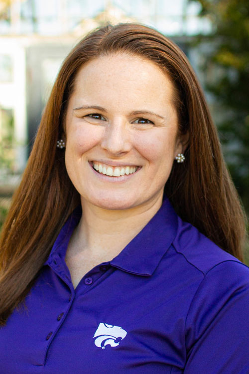 A woman in a purple shirt smiles for a portrait.