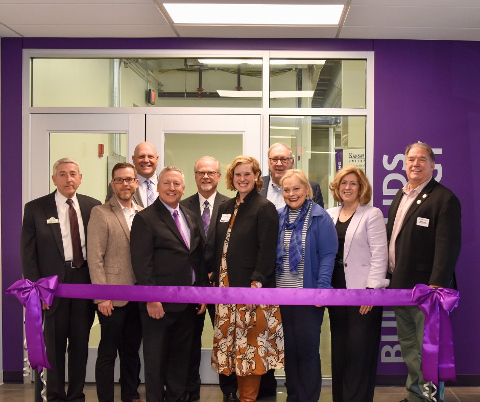 A group of university administrators pose for a group photo behind a purple ribbon.