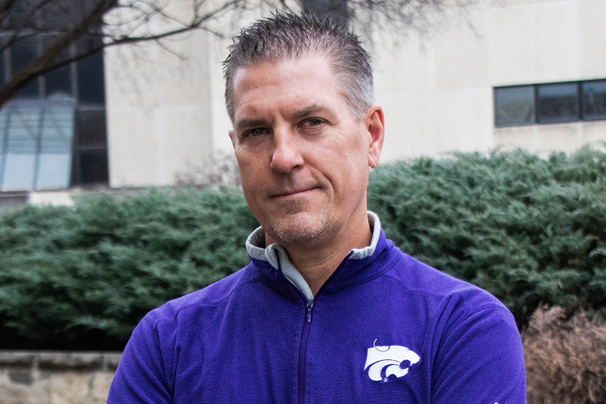 A male college professor in a purple polo poses for an outdoor portrait on a gloomy day.