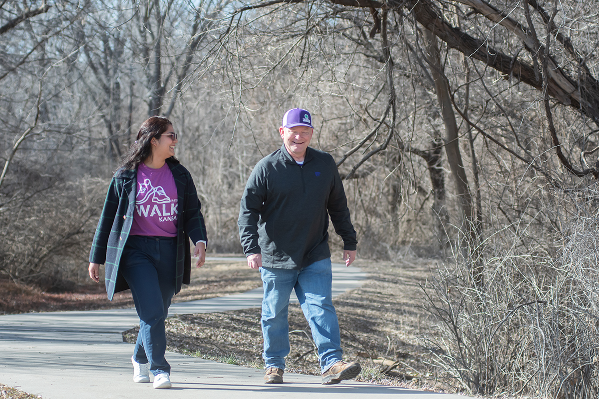 A woman and a man, dressed for cooler weather, walk along a pathway under leafless trees.