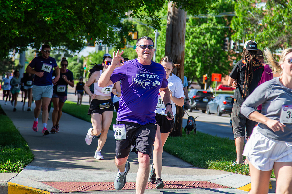 A man in a purple T-shirt and shorts runs in a race on a college's sidewalk.