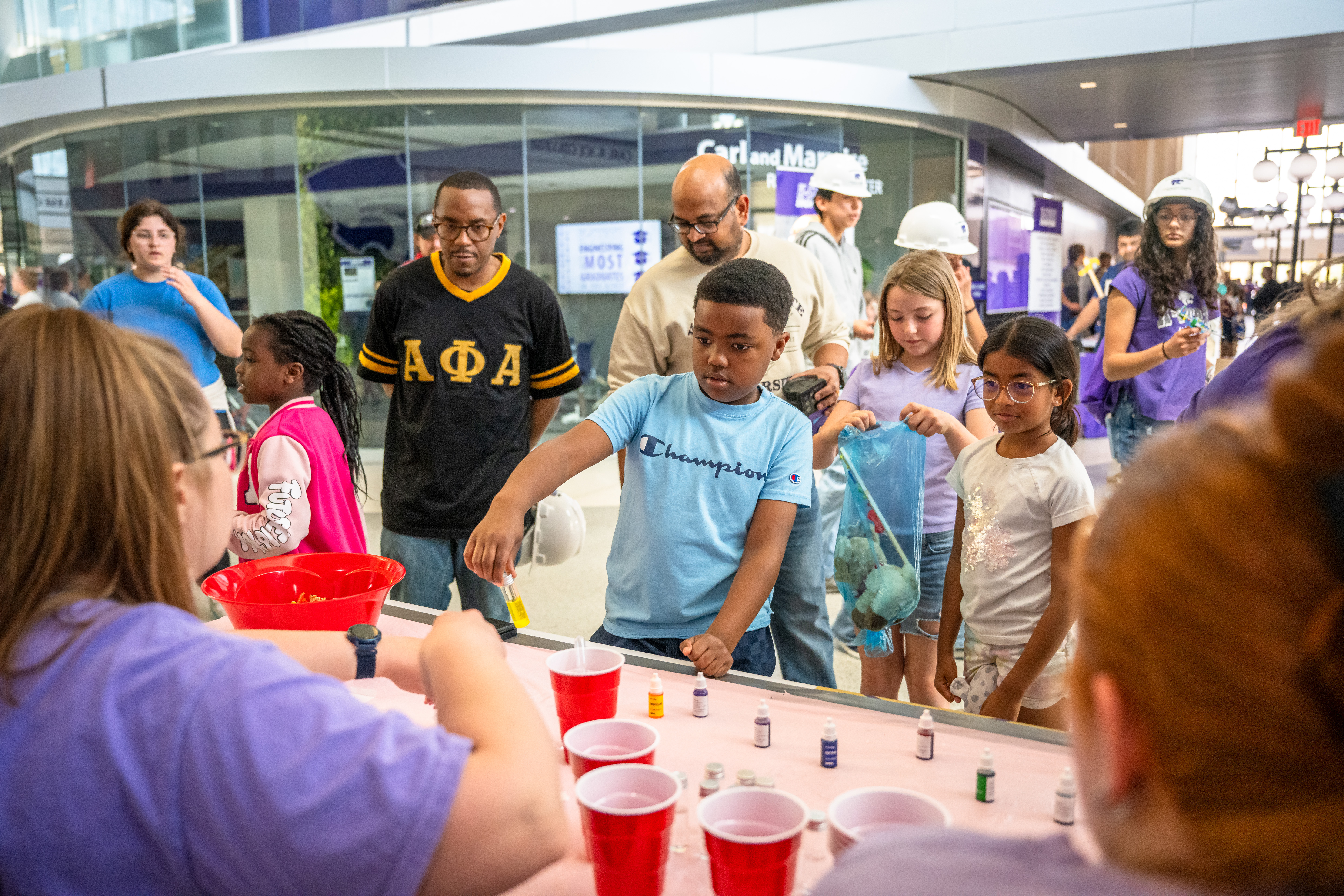 A group of community members stands around a table set up with solo cups and food dye for an experiment at Open House.
