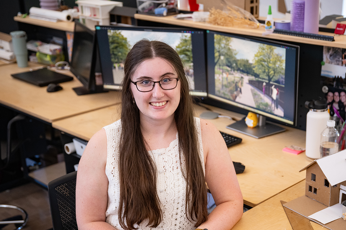 A female architecture graduate student sits at her desk and poses for a portrait.