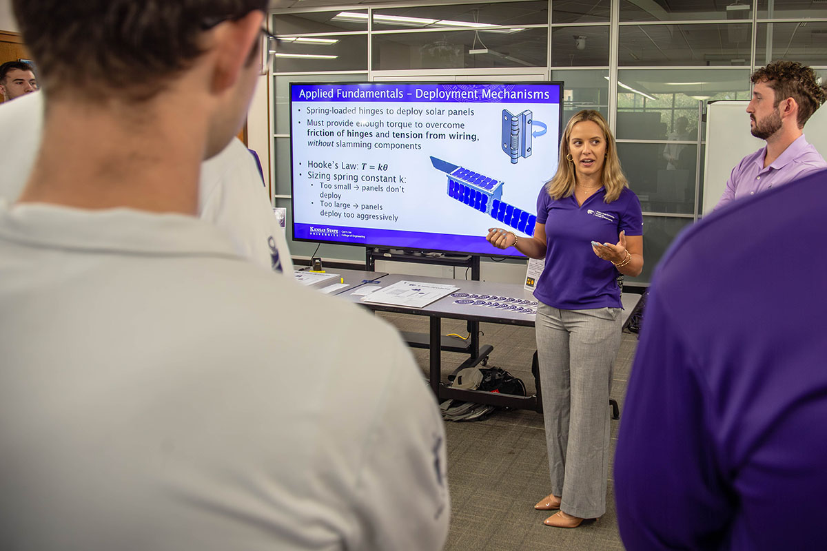 Two college students present about their satellite building work inside a classroom area at a college open house.