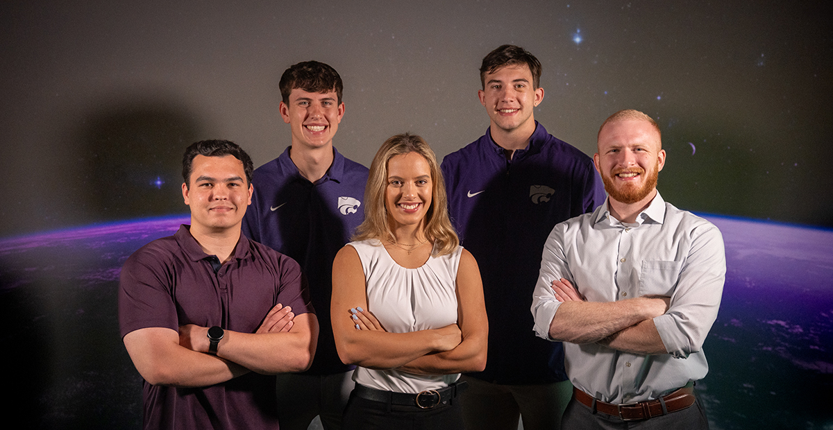 Five seniors in college gather for a group portrait in front of a backdrop of Earth.