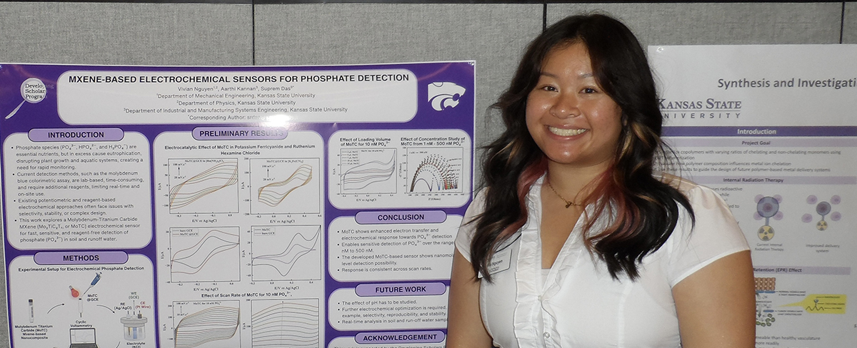 A student wearing a white blouse stands in front of a board that has a research poster posted on it.