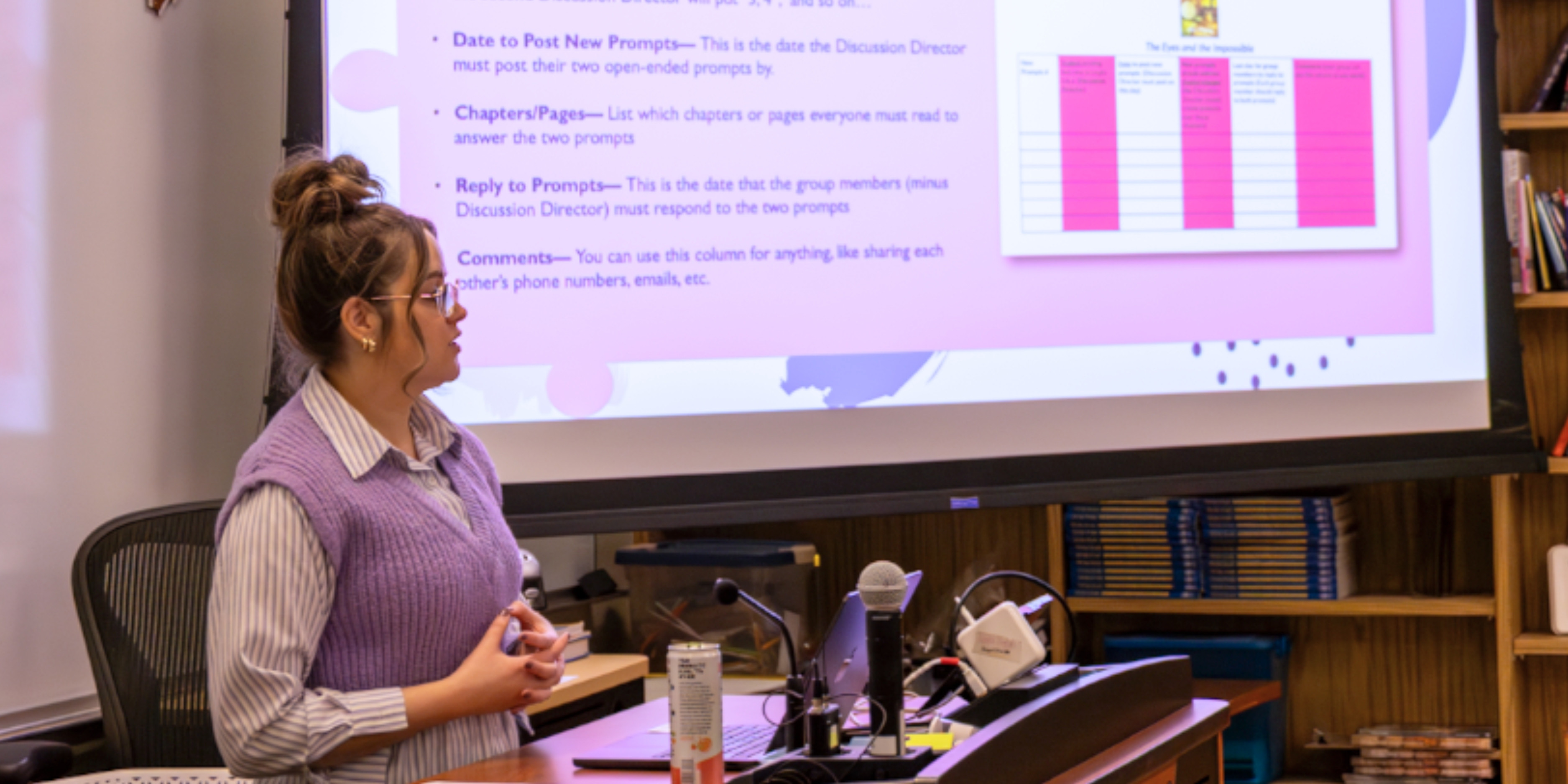 Kayln Hoppe presents at the front of a classroom. The slideshow shows a purple and pink graph with "Literature Circle Reading Schedules" visible.