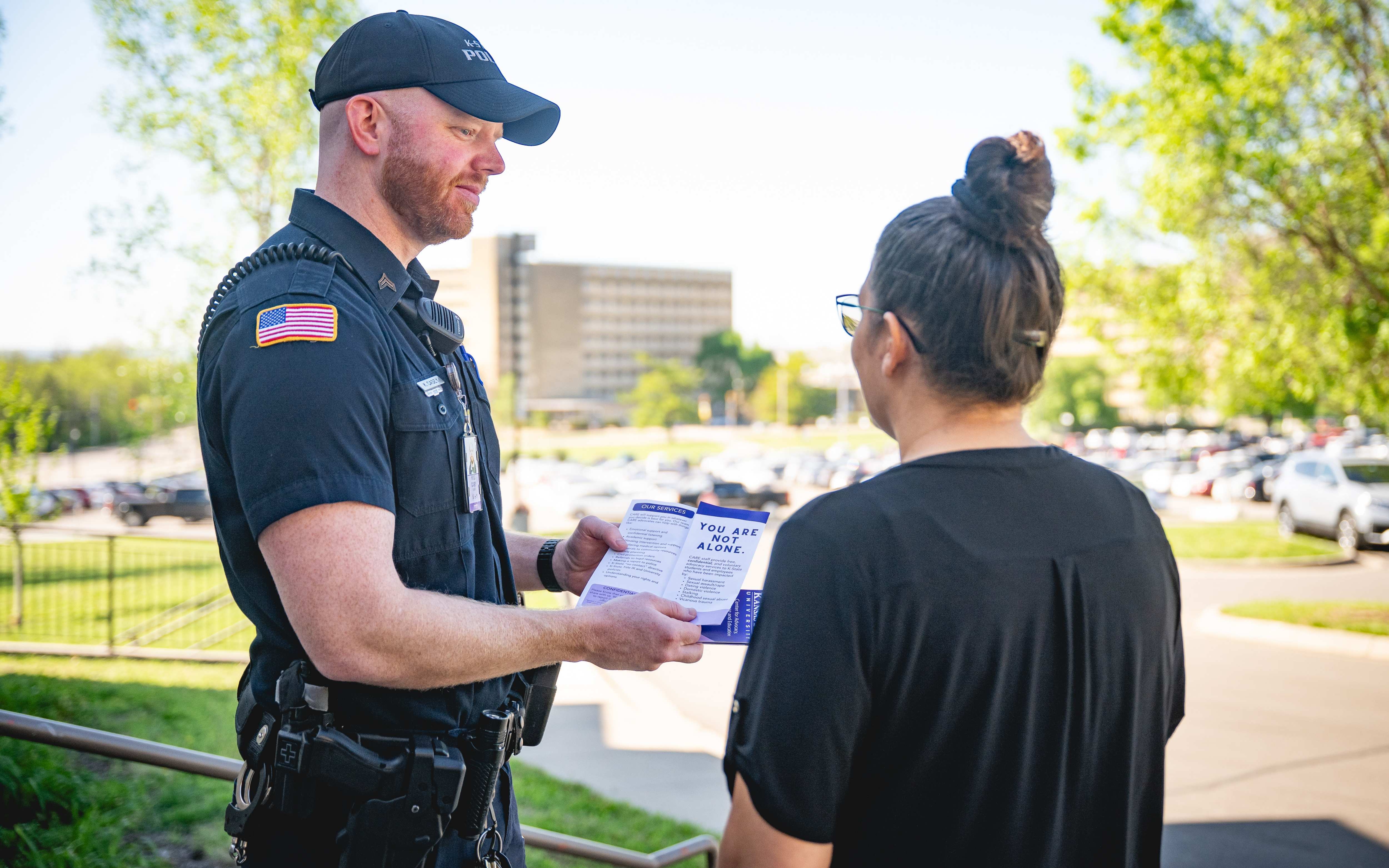 Kyle Casey stands explaining a pamphlet to a woman outside the K-State police station. Visible are the words "You are not alone."