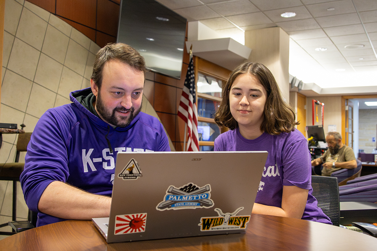A doctoral student and a college student sit at a desk and look at historic materials.