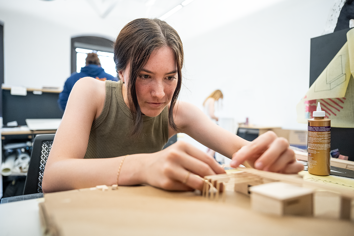 A female college student works on building a small-scale architectural model out of cardboard.