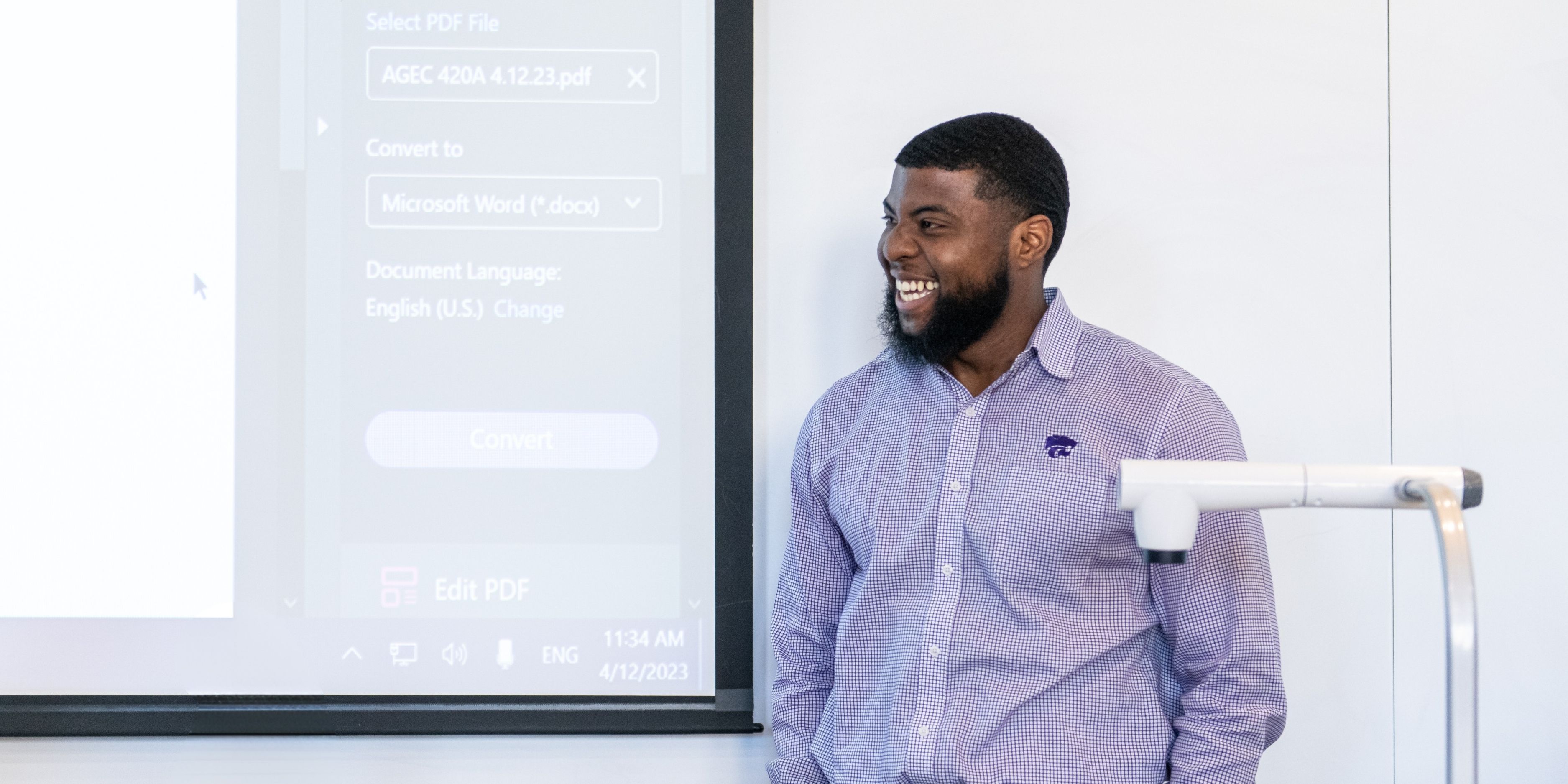 A man in a purple K-State long-sleeved collared shirt smiles and laughs while receiving his presidential award in 2023.
