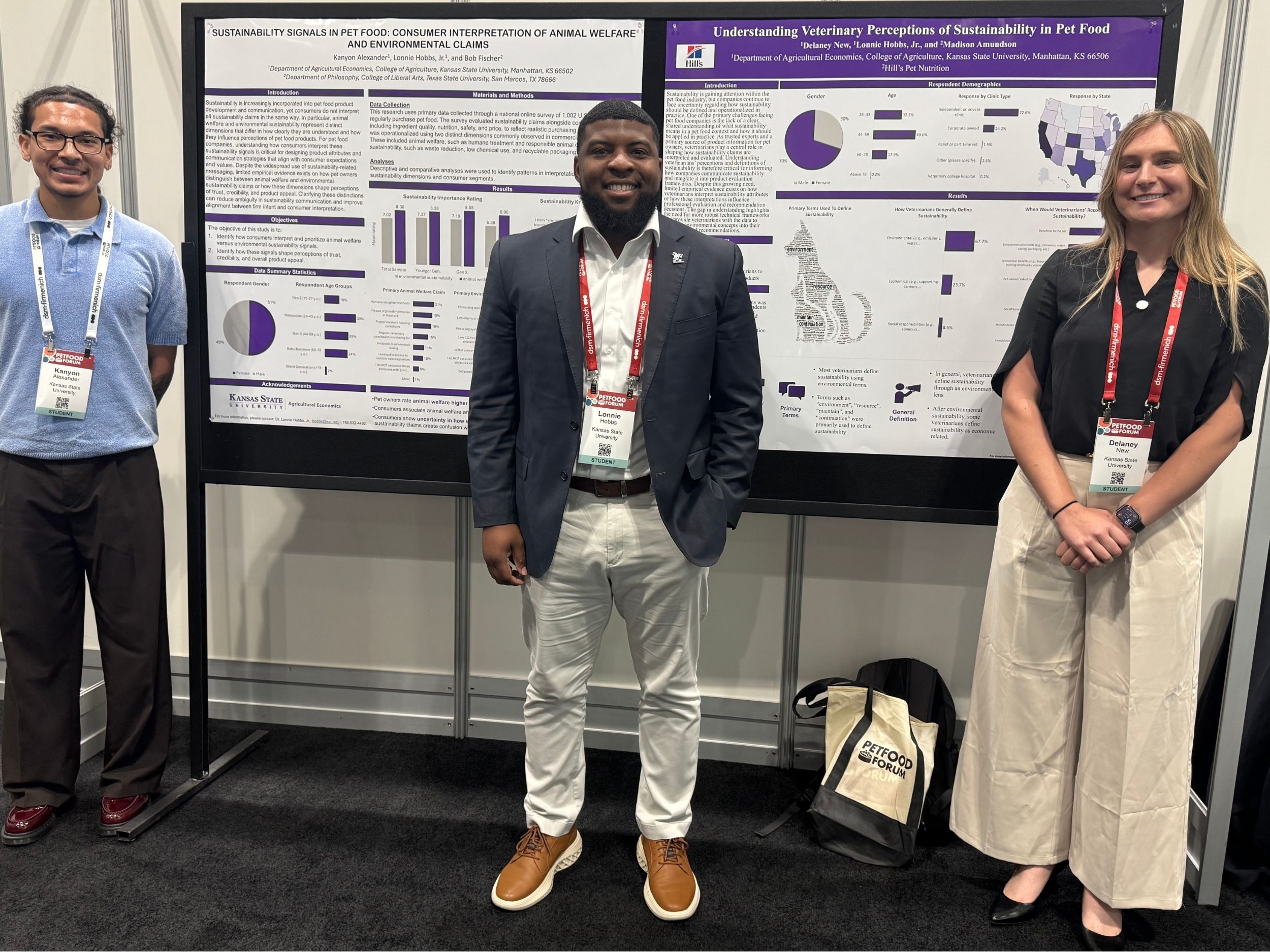 A professor stands and smiles with two students in front of research posters at a conference.