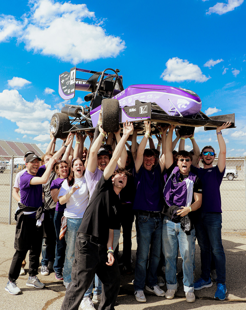 A group of people celebrating a win hold up a purple Formula SAE car.