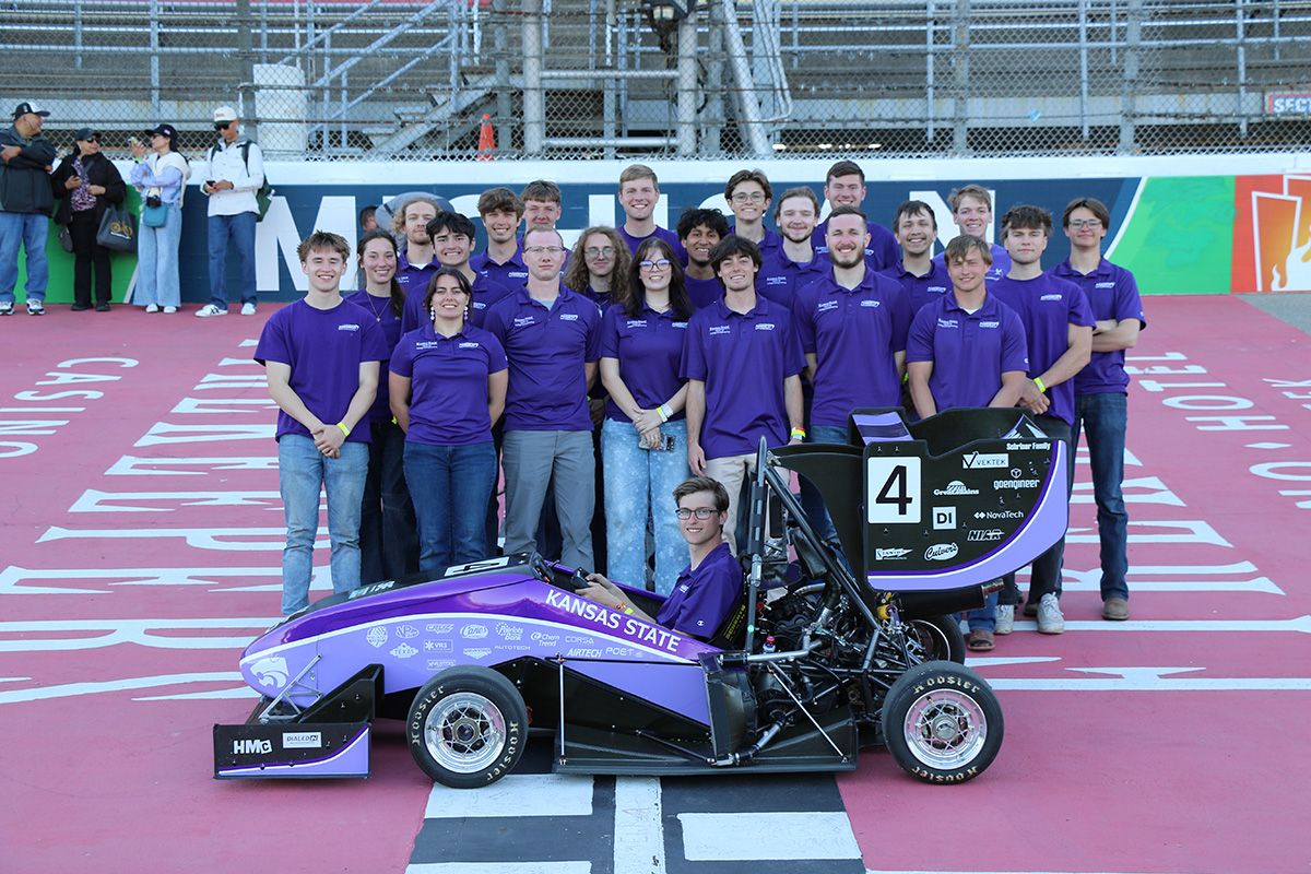 A group of young adults wearing purple polos stands behind a purple Formula SAE car.