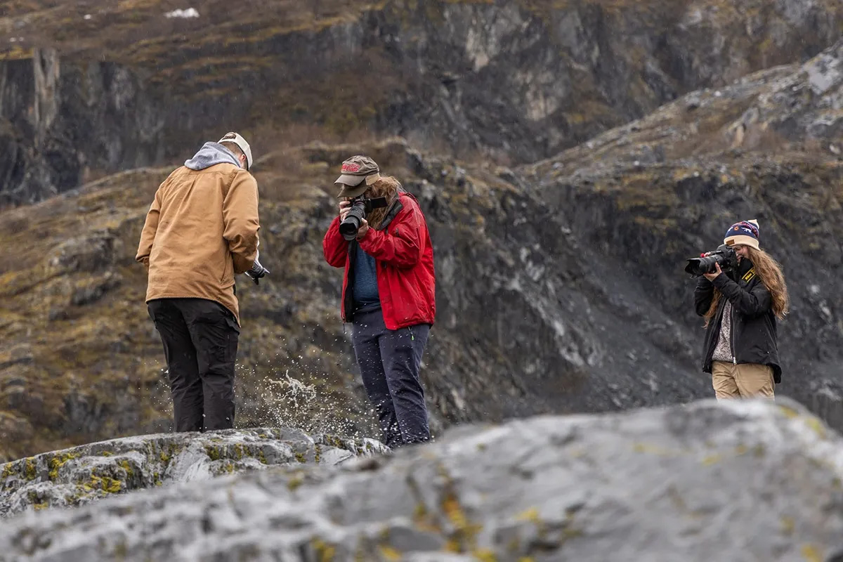 Three college students stand on a glacier in Alaska and take photos. 