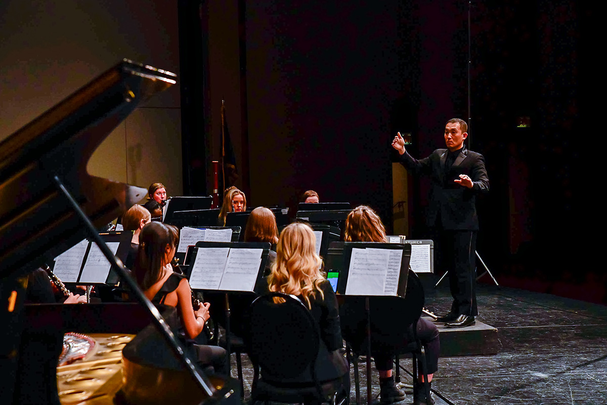 Alex Wimmer conducting a band on a concert stage. 