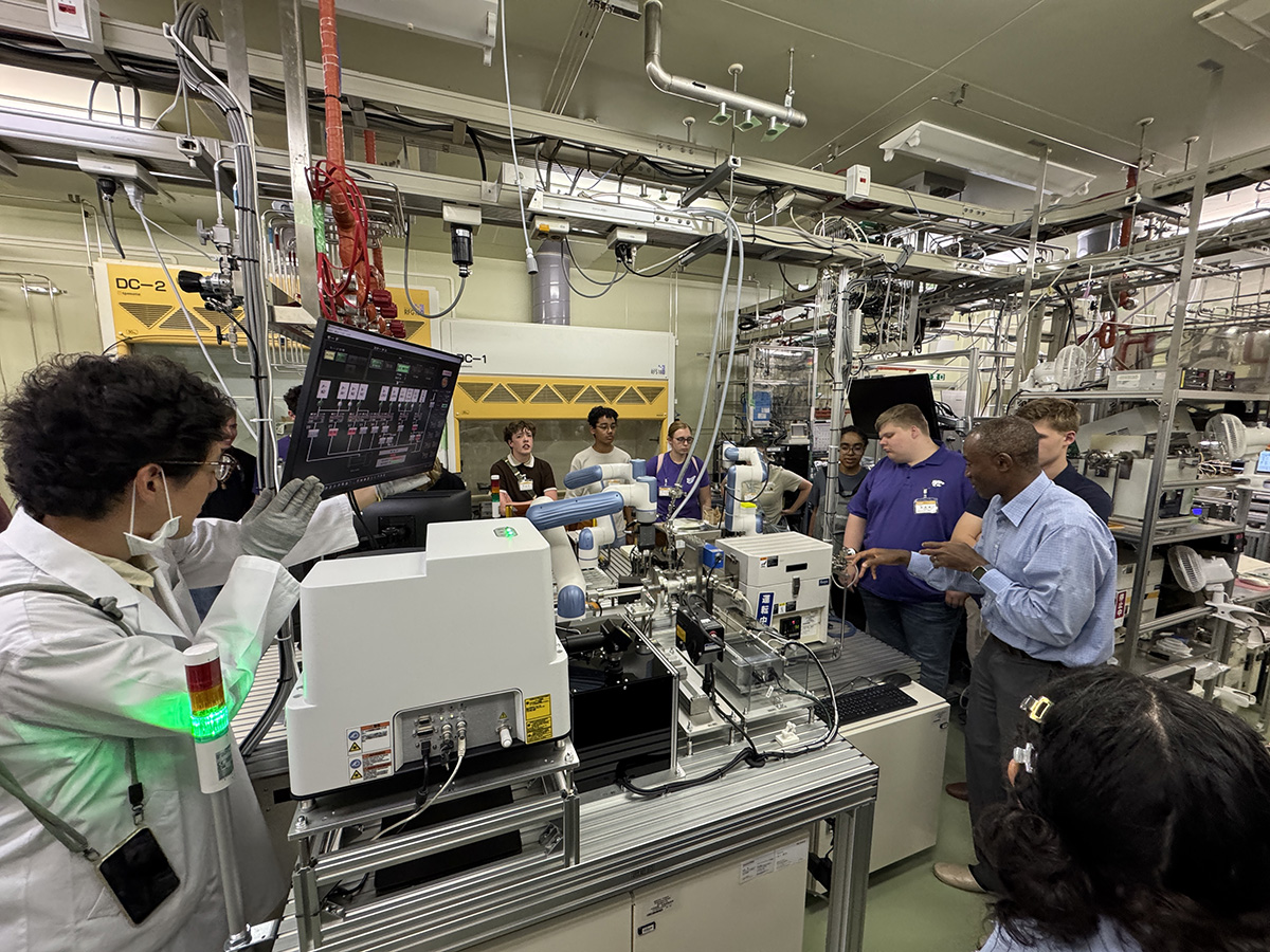 Students and professors are in a lab filled with tubing, wiring and a machine on a table.