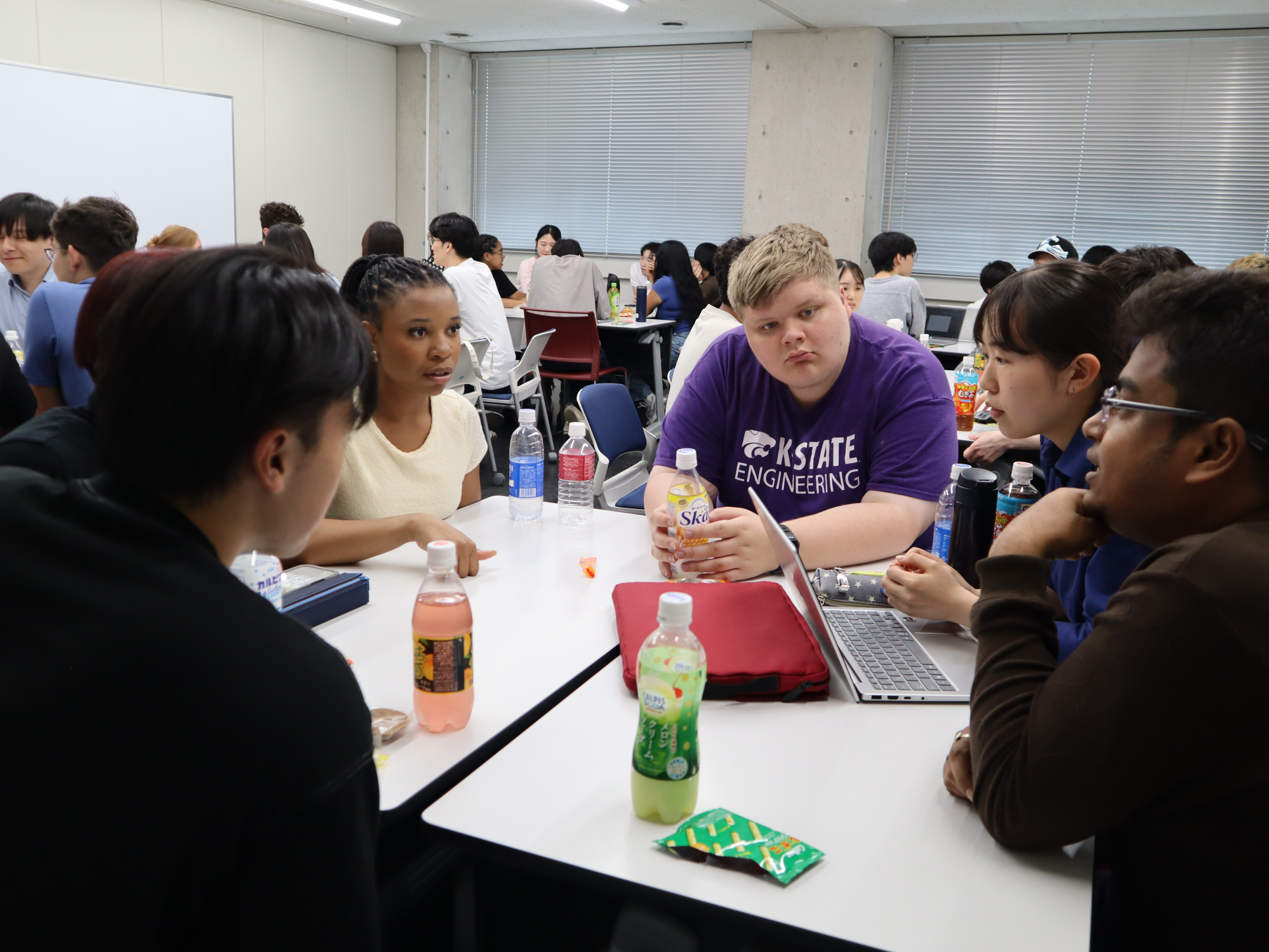 Students sit around tables talking.