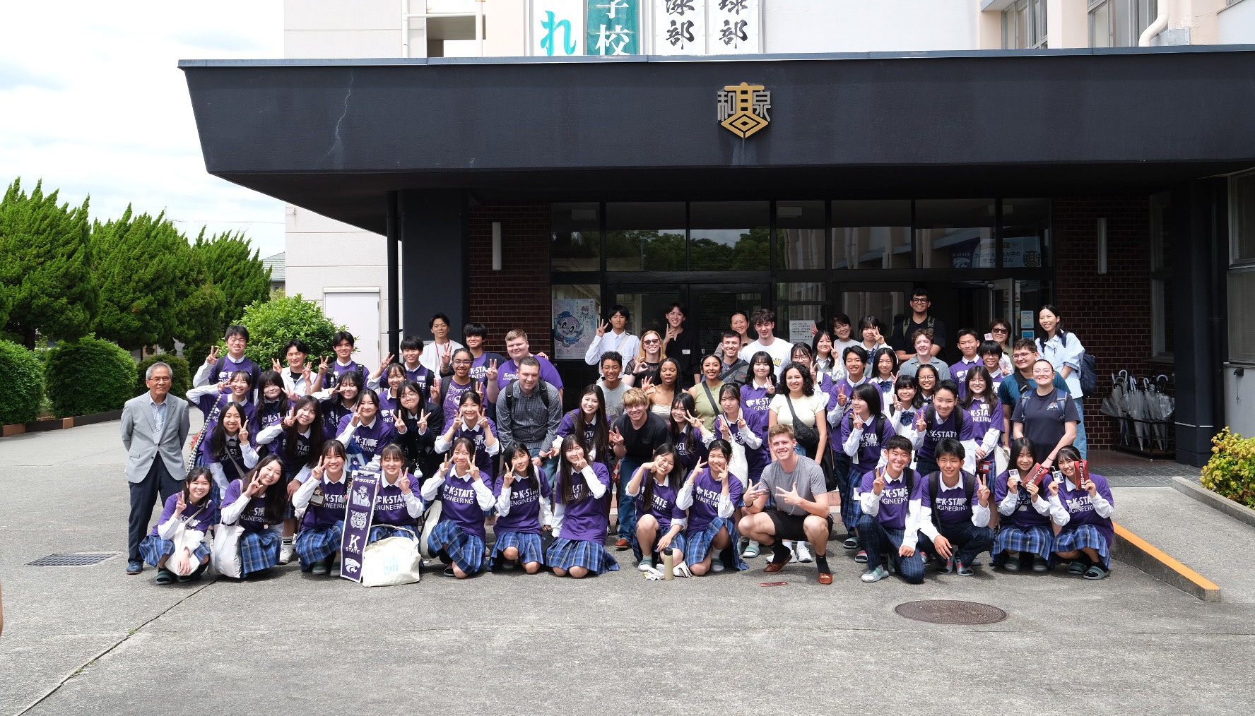 A large group of students wearing purple pose for a group photo in front of a building.