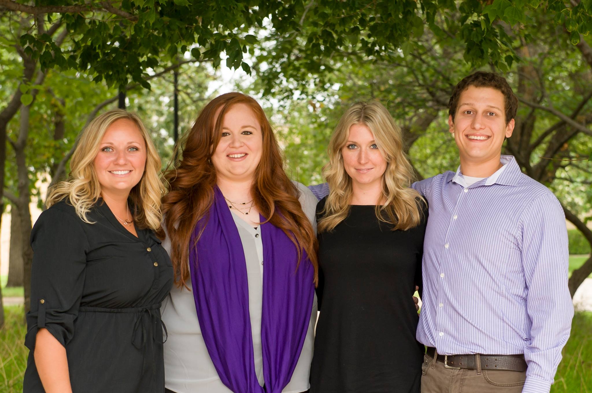 Four college graduate students stand together outside for a professional portrait.