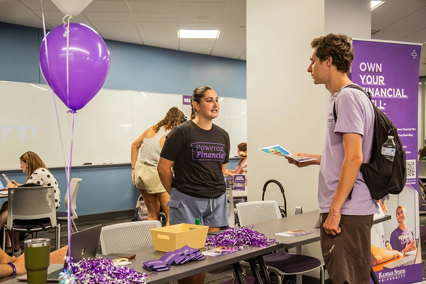 A student talks to a person at a table filled with purple giveaways.
