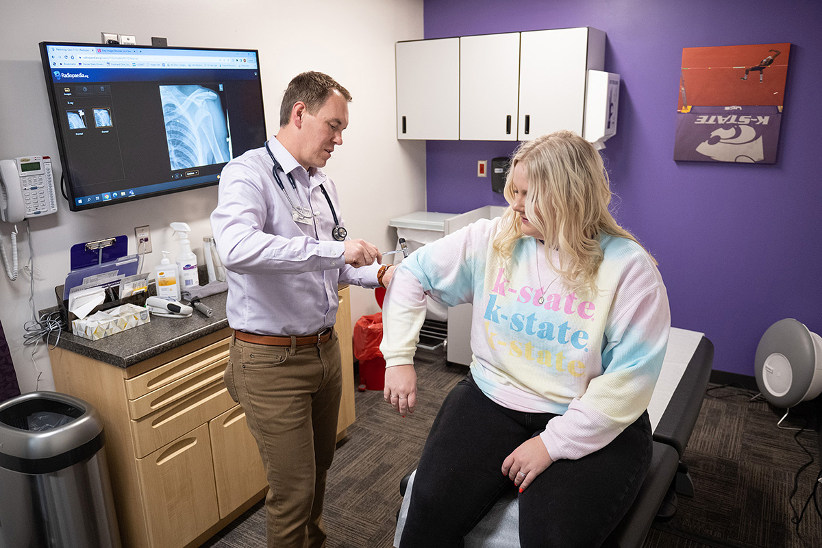A healthcare provider takes the blood pressure of a college student in an exam room. 