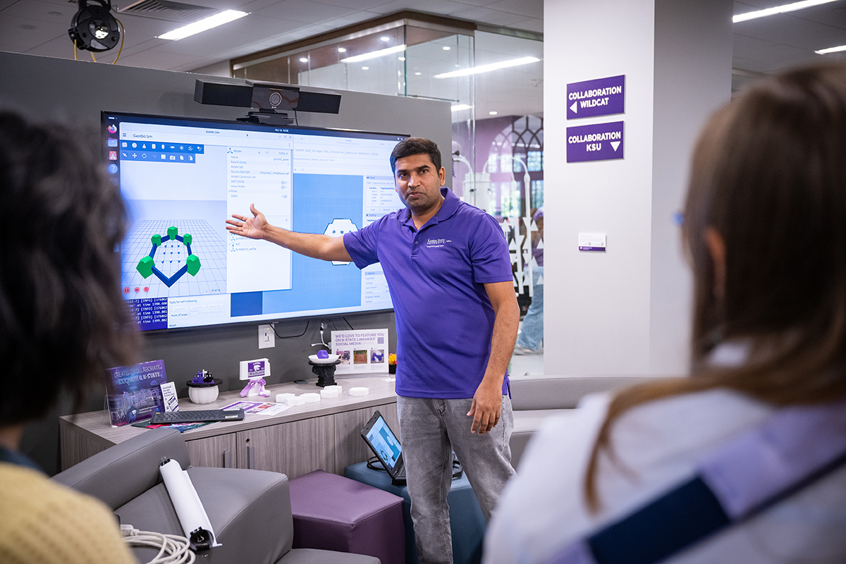A man in a purple polo stands in front of a screen and points to a graphic.