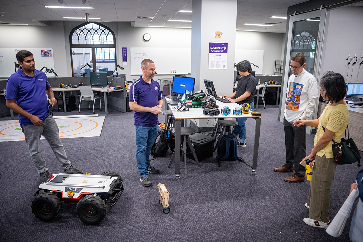 A group of people stands in a room with various robotics equipment around and on the ground.
