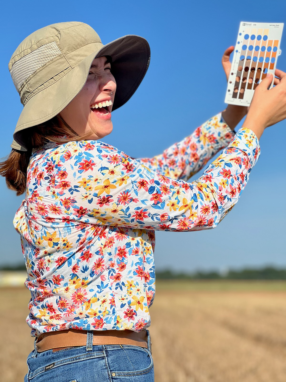 A student wearing a colorful floral shirt smiles and holds up a piece of paper with many colors and holes to compare object color.