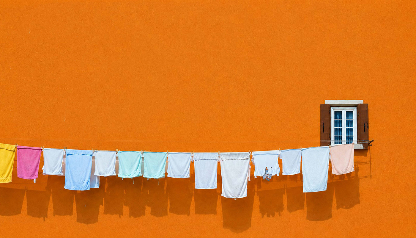 Several pieces of laundry hang from a clothesline against a bright orange wall and a brown-framed window. 