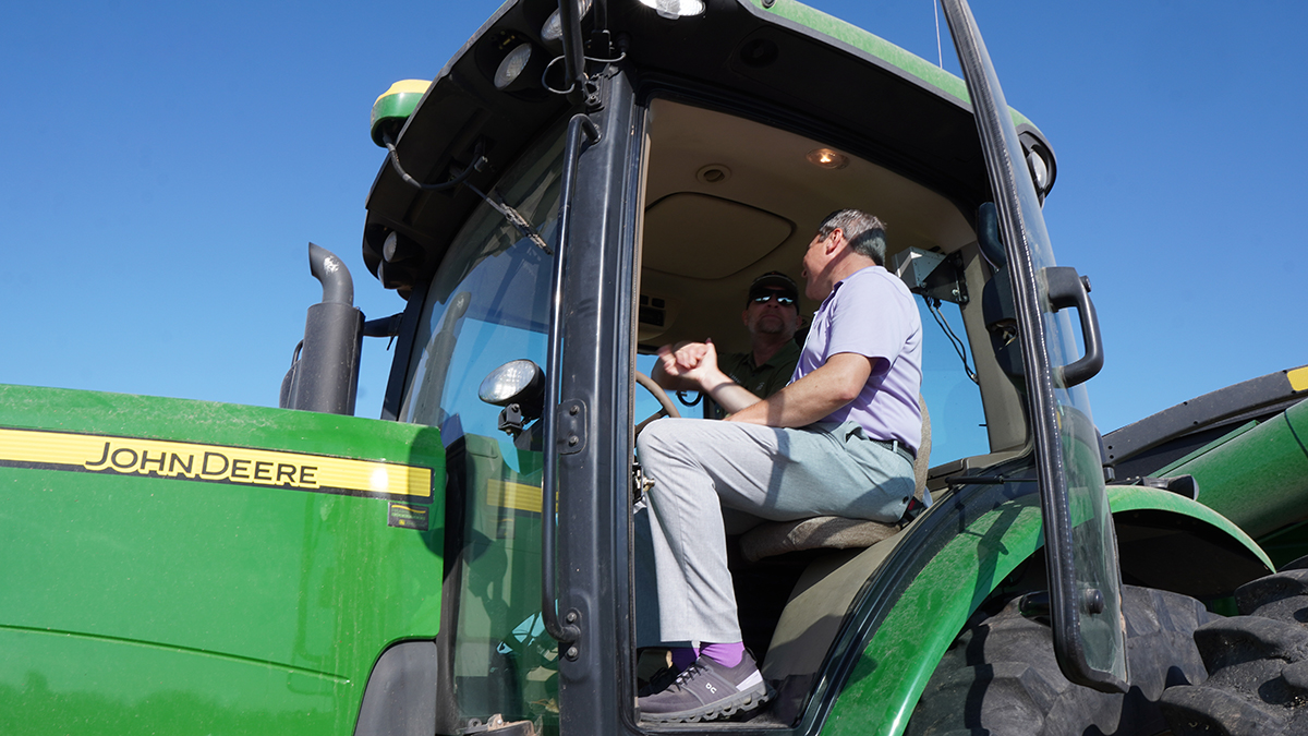 A close-up shot of two men sitting in a tractor shaking hands.