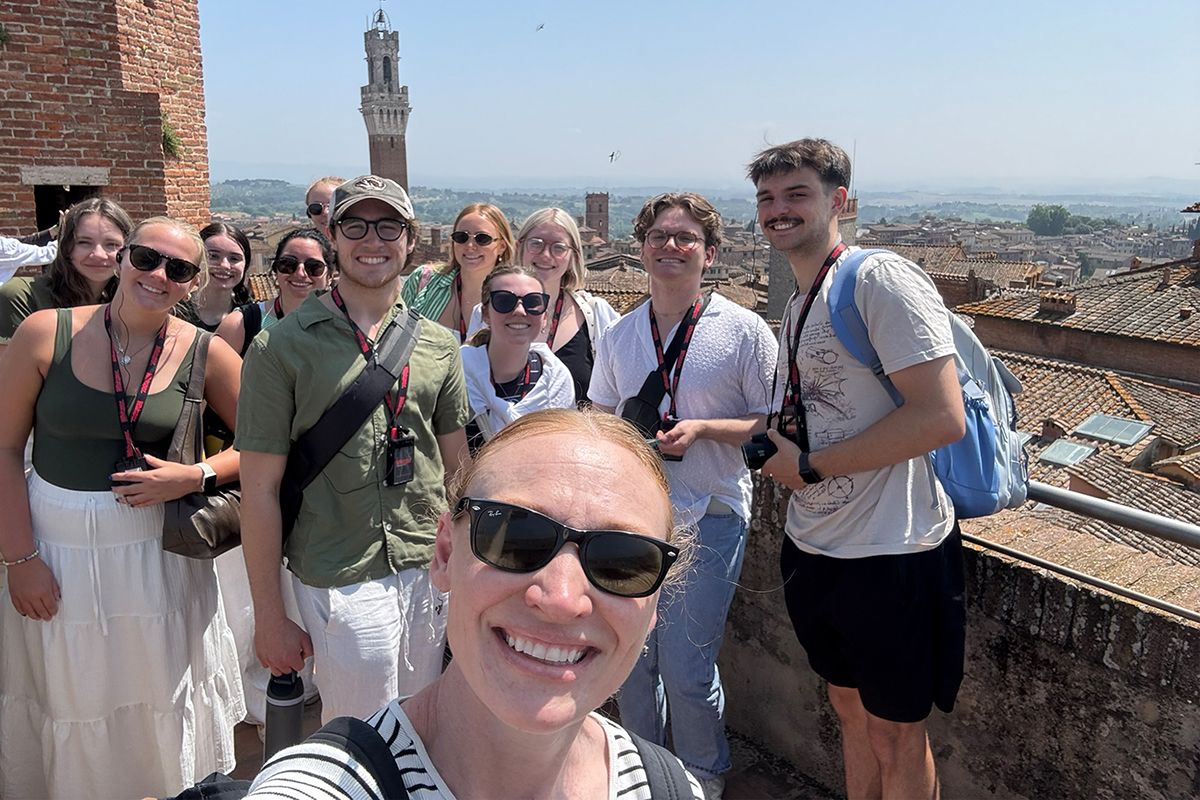A college professor poses for a selfie with a group of students.
