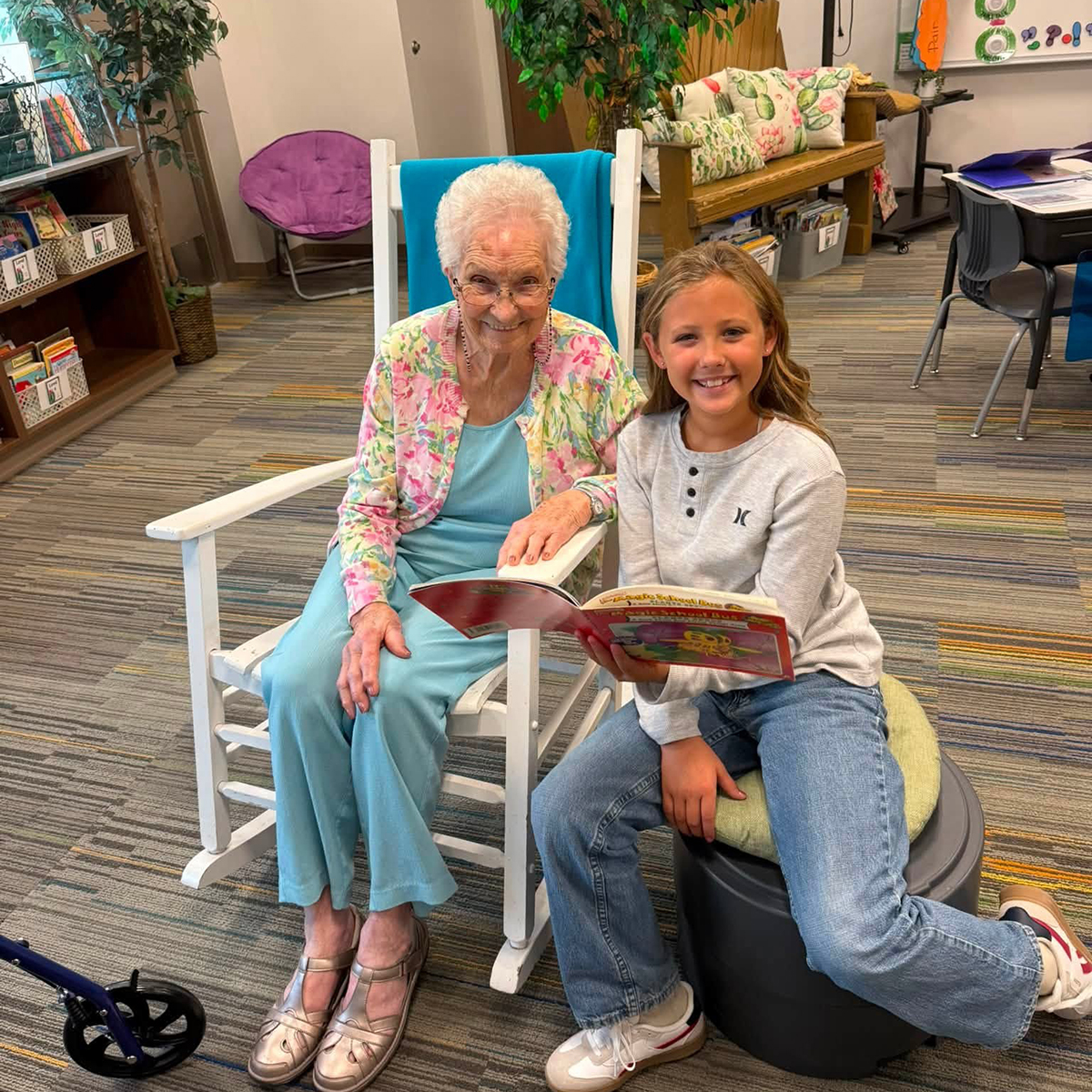 A senior woman and a young girl read together in a nursing home.