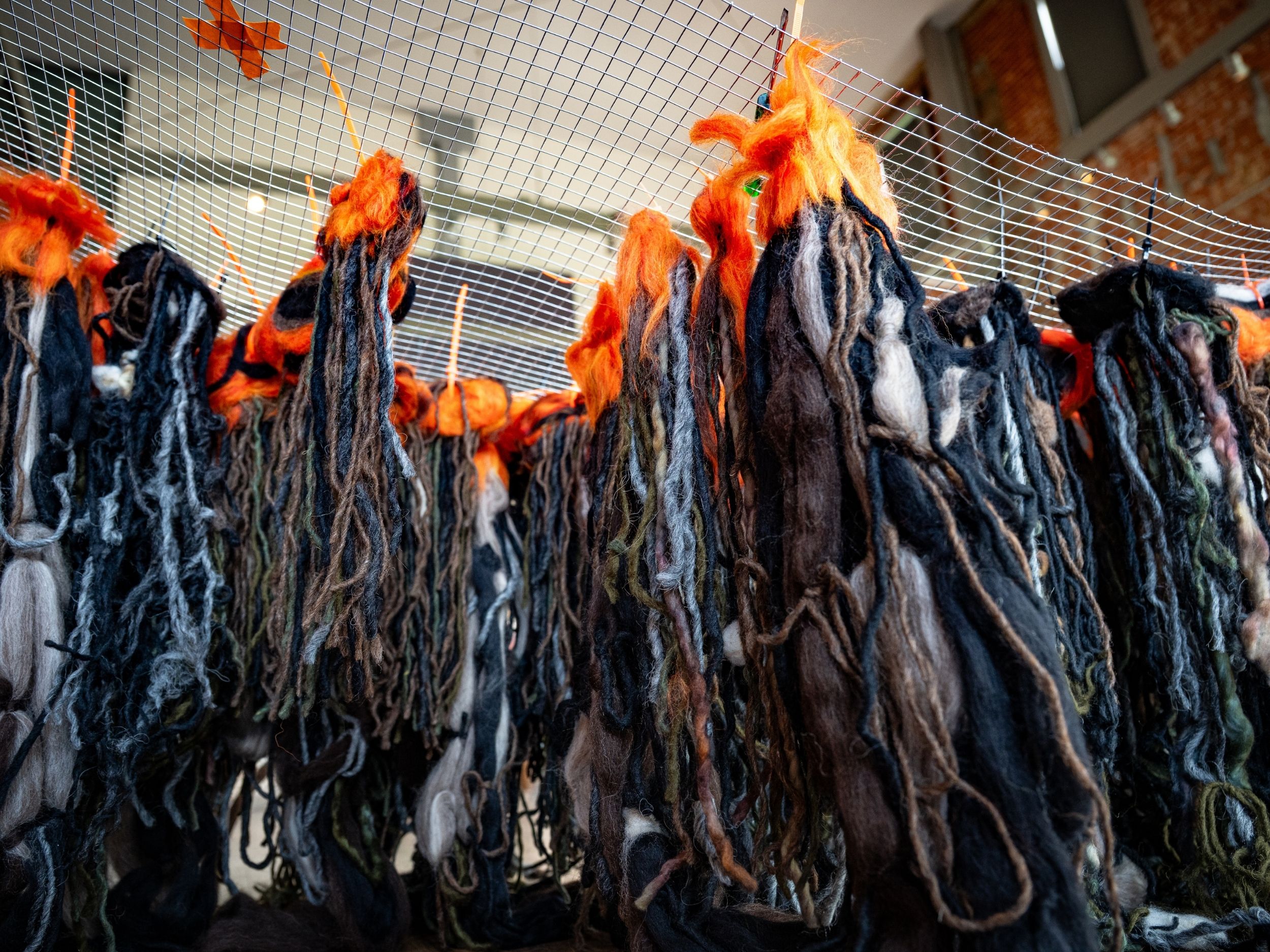 Bunches of black yarn with a orange yarn ball at the top, tied to a wire frame using zip ties