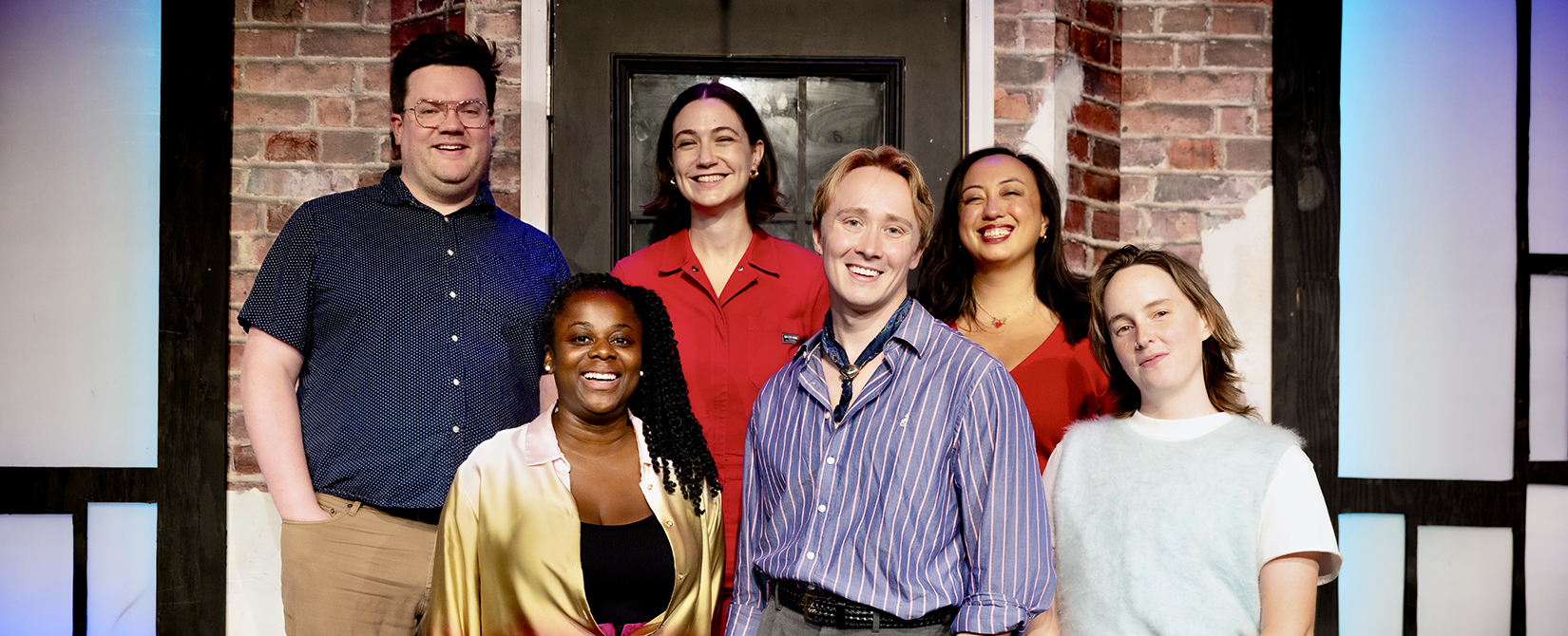 A group of six people stand in front of a brick wall background.