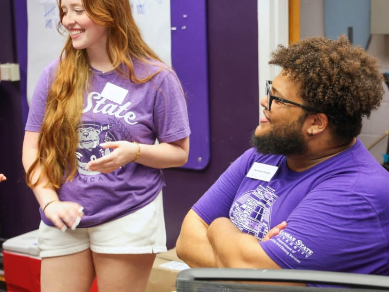 Nathan Dozier sits behind a desk in a residence hall, speaking and laughing with resident assistants during move in.