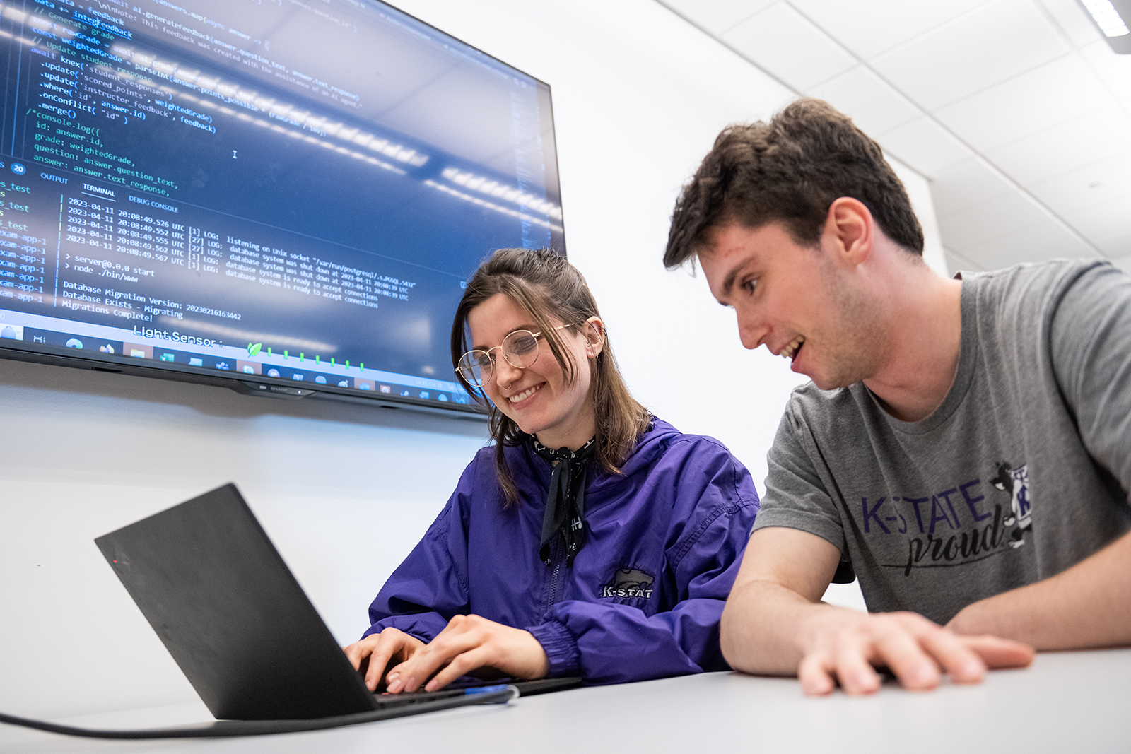 A female student and a male student sit at a desk and work on a laptop.