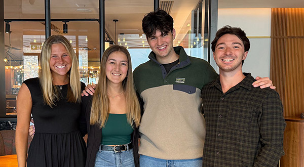 A group of two women college students and two men college students stand in a line for a group portrait.