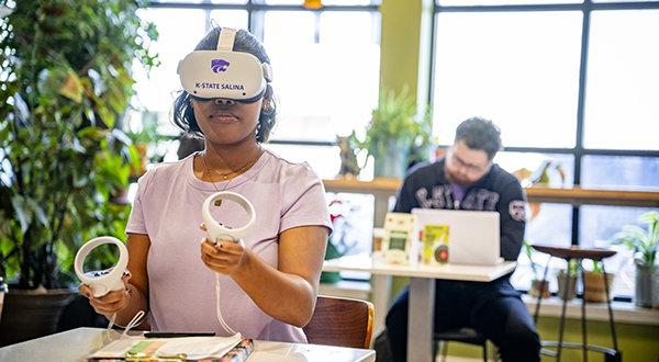 A student sits at a cafe table and interacts with a virtual reality headset.