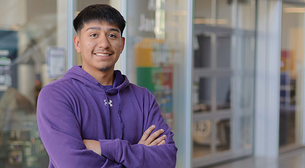 A student in a purple hoodie poses for a portrait in front of a glass-walled engineering garage.