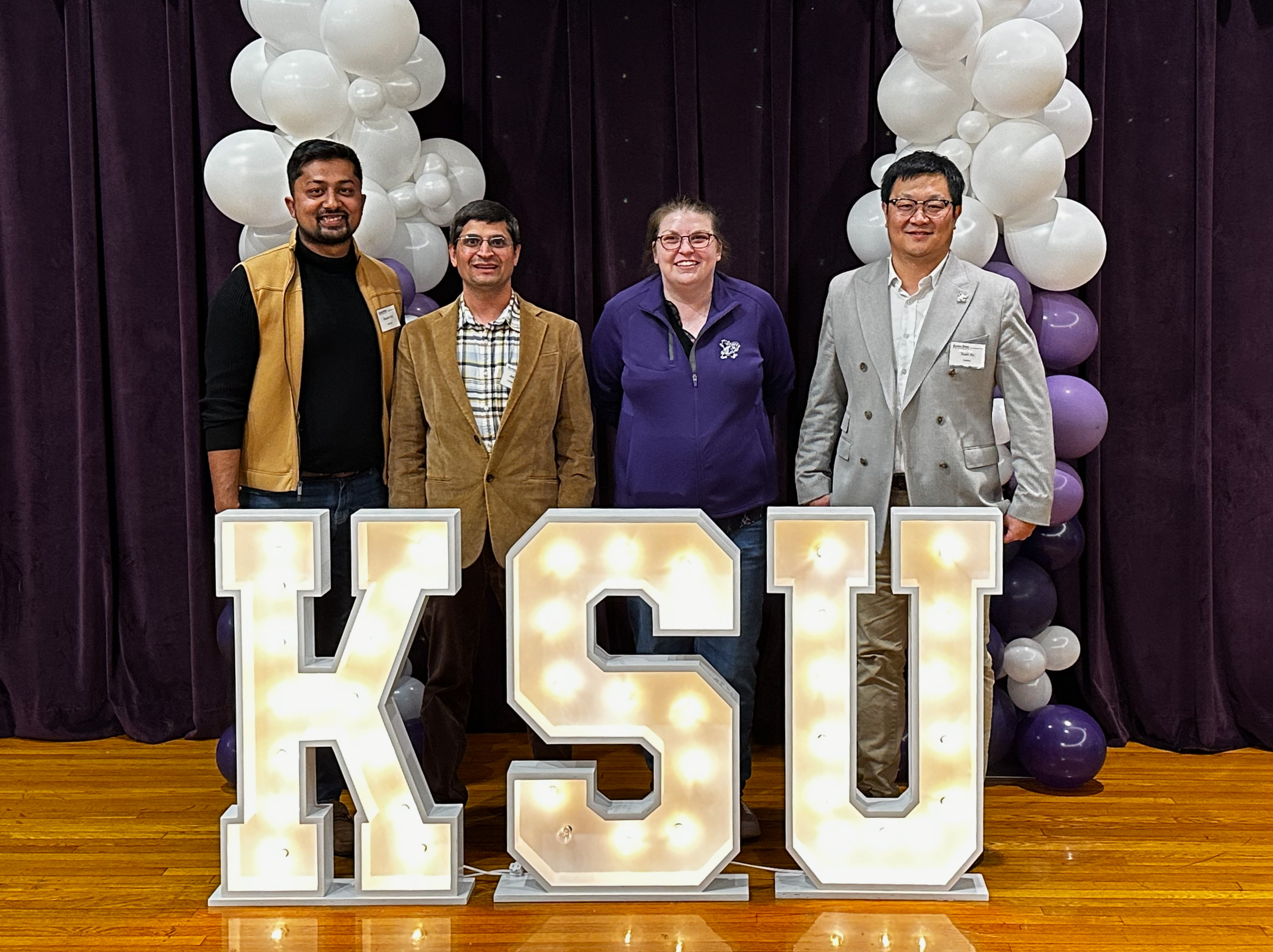 Four faculty members standing behind lit-up KSU letters