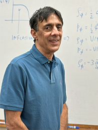 A man in a blue polo in front of a whiteboard with equations on it.