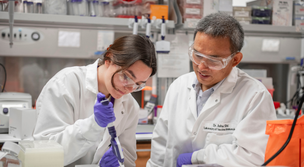 A researcher works with a student in a lab.