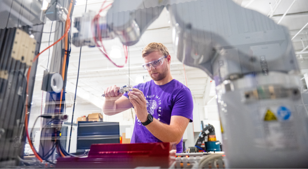 An engineering student works with a robotic arm.