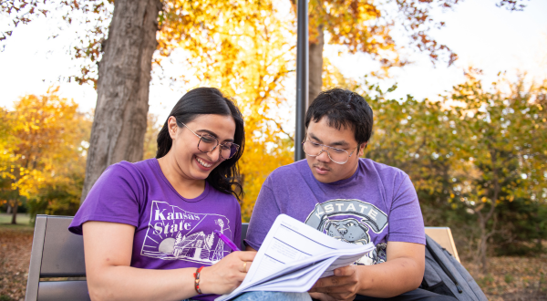 Two students sit on a bench looking at a notebook.