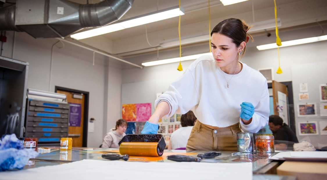 A girl uses a paint roller to begin a printmaking project