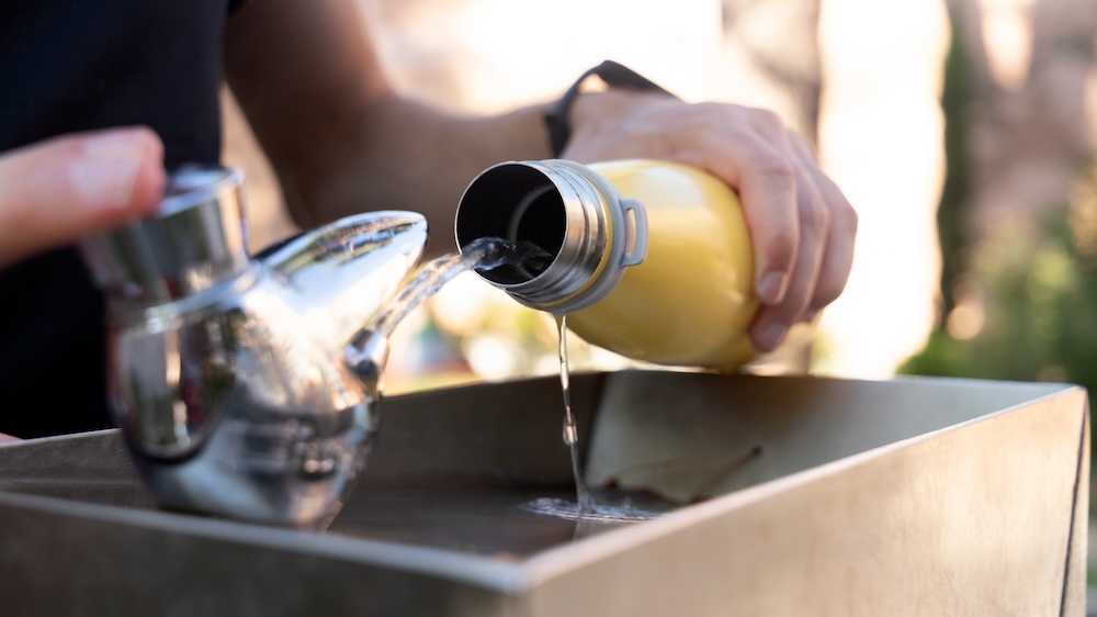 A closeup of a metal water bottle being refilled at a fountain