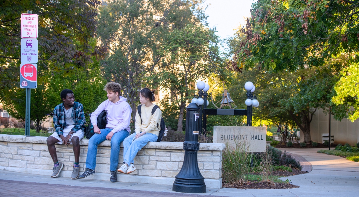 Three students sitting on a limestone wall outside of Bluemont Hall