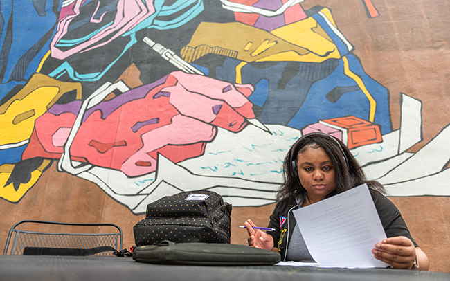 Student working on classwork in front of a colorful mural